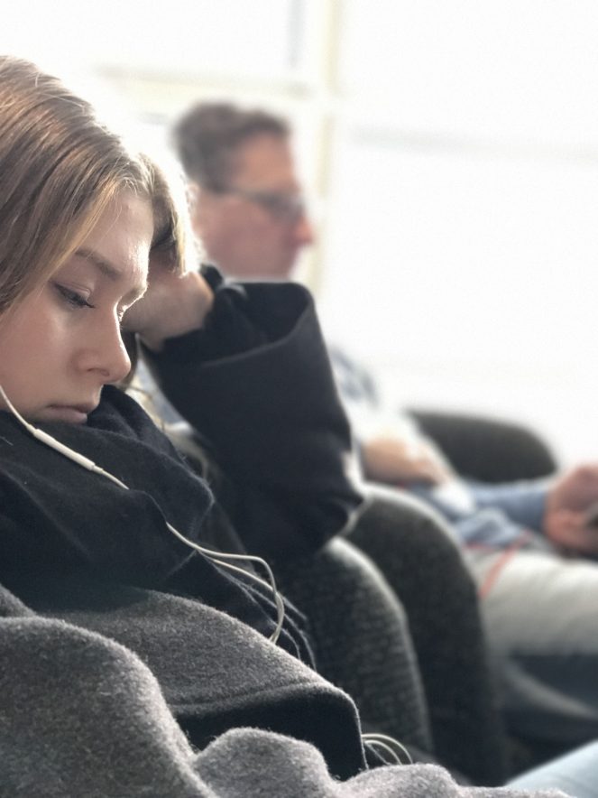 a young woman waiting in a chair at the airport. Not in the celebrity lounge. 